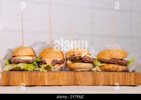 Quatre hamburgers avec cure-dents dedans. Les hamburgers sont sur une planche de bois Banque D'Images