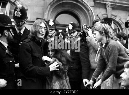 John Lennon protège Yoko Ono après que la foule a essayé de les agresser après qu'ils ont quitté un tribunal de Londres pour entendre des accusations de possession de marijuana et d'obstruction à la police. Le couple a été libéré sous caution de £100 jusqu'à leur procès le 28 novembre. Londres - 19 octobre 1968 Banque D'Images