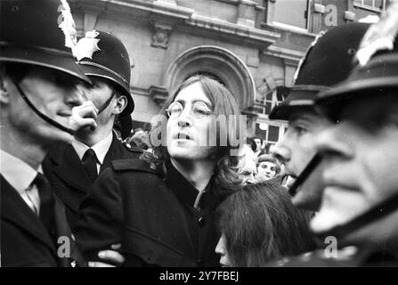 John Lennon protège Yoko Ono après que la foule a essayé de les agresser après qu'ils ont quitté un tribunal de Londres pour entendre des accusations de possession de marijuana et d'obstruction à la police. Le couple a été libéré sous caution de £100 jusqu'à leur procès le 28 novembre. Londres - 19 octobre 1968 Banque D'Images