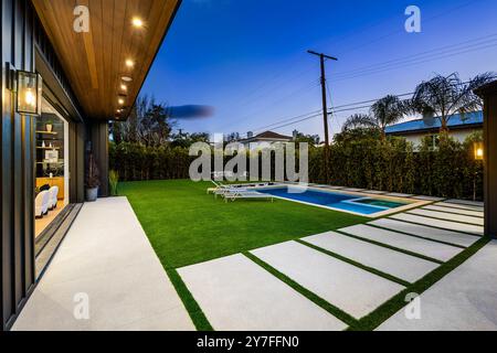 Jardin moderne avec piscine et pelouse bien entretenue au crépuscule, avec mobilier d'extérieur contemporain et éclairage d'ambiance. Banque D'Images