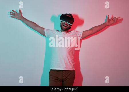 Homme heureux dans des lunettes de réalité virtuelle gestuelle avec des ombres colorées en arrière-plan Banque D'Images