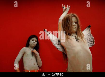 Deux sœurs recouvertes d'argile, dont l'une porte des ailes, posent devant un mur rouge à Sayulita, au Mexique. Banque D'Images