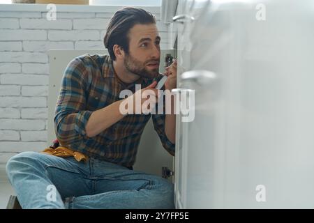 Jeune homme confiant à l'aide d'une clé tout en réparant un évier à la cuisine domestique Banque D'Images