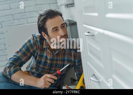 Jeune homme confiant réparant des meubles à la cuisine domestique Banque D'Images