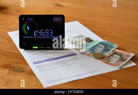 Compteur intelligent d'électricité en affichage à la maison (IHD) sur la table en bois montrant le coût mensuel et l'utilisation en kilowattheures (kWh) Banque D'Images