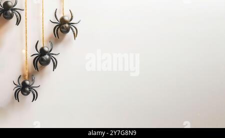 Spooky Halloween petites décorations d'araignée en faux plastique noir suspendues à des fils d'or isolés sur un fond clair blanc cassé, neutre, Banque D'Images