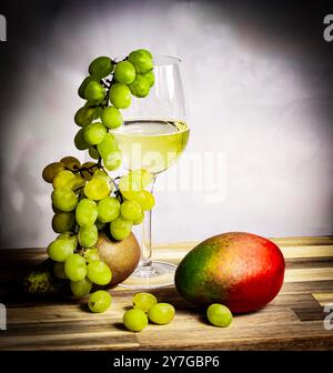 Composition de nature morte avec un verre de vin blanc avec des raisins verts, mangue et poire sur une surface en bois - une scène fraîche et élégante. Banque D'Images