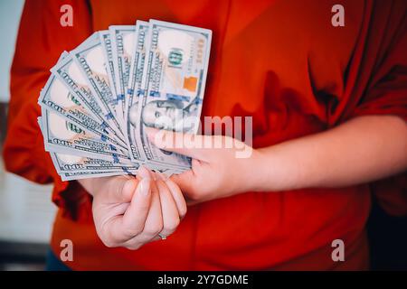 Gros plan détaillé des mains tenant soigneusement un éventail de billets de cent dollars dans une position idéale Banque D'Images