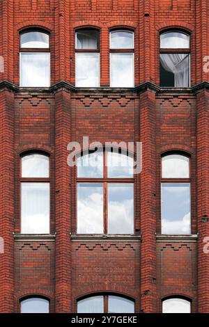 La remarquable façade en briques rouges de Mitte, Berlin, présente de grandes fenêtres reflétant le ciel et témoignant du riche patrimoine architectural. Banque D'Images