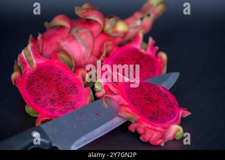Fruits de dragon vifs et frais magnifiquement tranchés et présentés sur une surface sombre, accompagnés d'un couteau Banque D'Images