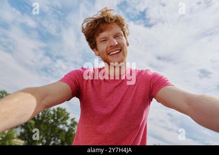 Beau jeune homme rousse faisant selfie et souriant tout en se tenant dehors Banque D'Images