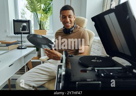 Confiant jeune homme multiracial tenant un disque vinyle tout en étant assis près de la platine Banque D'Images