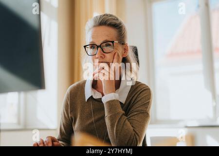 Femme d'affaires mûre réfléchie avec des lunettes appuyées sur le coude au bureau Banque D'Images