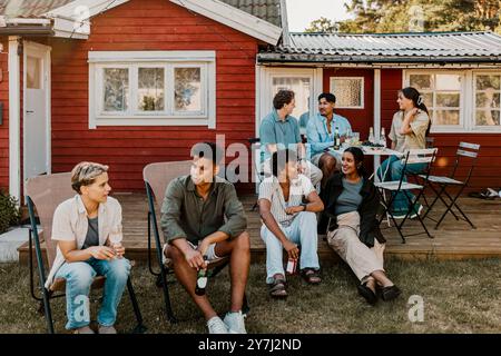 Groupe multiracial d'amis masculins et féminins assis et parlant les uns avec les autres tout en étant assis dans la cour arrière à PA social Banque D'Images