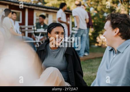 Heureuse jeune femme parlant avec un ami masculin tout en étant assise dans la cour arrière Banque D'Images