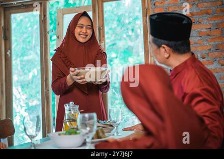 Maman musulmane asiatique apporte un bol de compote pour l'iftar de la famille Banque D'Images