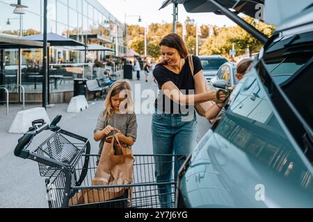 Femme souriante chargeant des sacs d'épicerie avec des fils dans le coffre de voiture au marché Banque D'Images