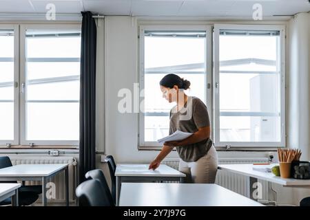 Professeure femme gardant les papiers d'examen sur le bureau tout en se tenant debout dans la salle de classe au collège Banque D'Images