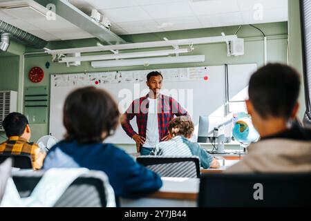 Enseignant masculin avec des armes akimbo groupe d'enseignement d'élèves assis en classe à l'école Banque D'Images