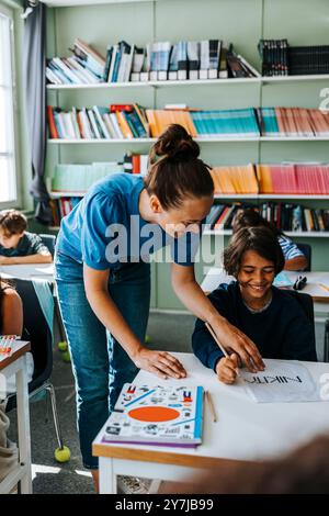 Professeur féminin aidant l'élève élémentaire avec créativité dans la classe de dessin à l'école Banque D'Images