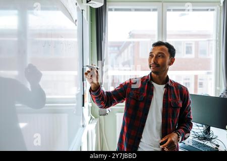 Enseignant masculin écrivant sur le tableau blanc avec un stylo feutre tout en se tenant debout dans la salle de classe à l'école primaire Banque D'Images