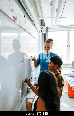 Enseignante aidant les élèves à dessiner le diagramme sur tableau blanc dans la salle de classe à l'école primaire Banque D'Images