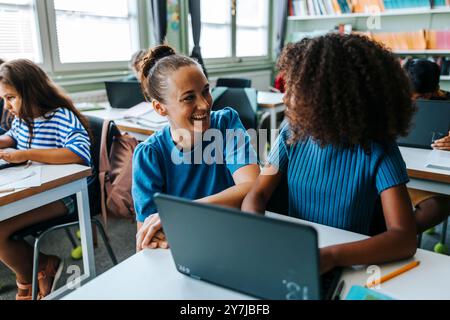 Heureuse professeure féminine à côté de l'élève de cheveux bouclés faisant e-learning en classe à l'école primaire Banque D'Images