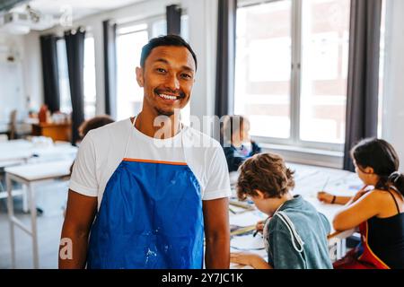 Portrait d'un professeur d'art masculin souriant portant un tablier bleu en classe à l'école Banque D'Images