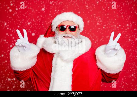 Portrait en gros plan de son beau Père Noël barbu joyeux et paisible montrant une ambiance festive double V-sgn isolé sur vif lumineux Banque D'Images