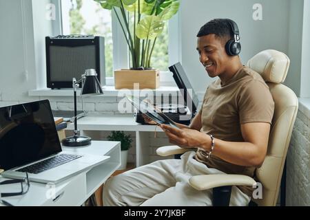 Bel homme dans les écouteurs examinant le disque vinyle tout en étant assis à son lieu de travail Banque D'Images