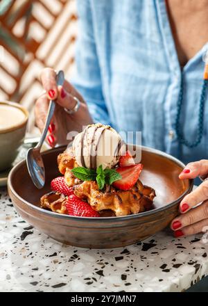 Femme mangeant des gaufres américaines avec de la crème glacée, des fraises, du sirop d'érable et des pépites de chocolat noir. Banque D'Images