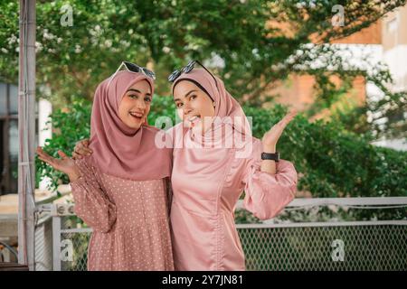 Deux femmes joyeuses habillées de hijabs roses posant ensemble à l'extérieur, rayonnant de joie Banque D'Images