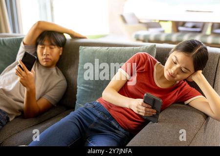 Détente sur le canapé, jeune frère asiatique et soeur à l'aide de smartphones dans le salon ensemble Banque D'Images