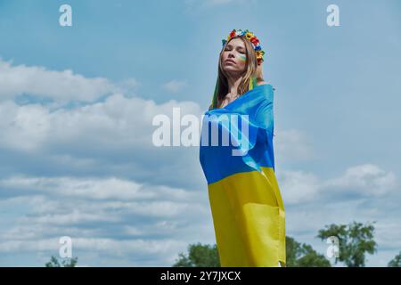 Belle jeune femme ukrainienne couvrant avec drapeau national avec le ciel en arrière-plan Banque D'Images