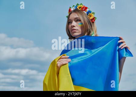 Belle jeune femme ukrainienne couvrant avec drapeau national avec le ciel en arrière-plan Banque D'Images