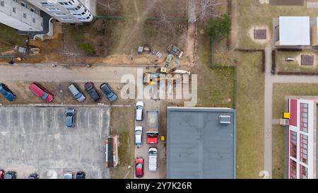 Vue aérienne d'un chantier de construction à proximité d'immeubles résidentiels. La machinerie lourde est stationnée sur une zone de terre, les ouvriers étant visibles. Plusieurs voitures sont lin Banque D'Images