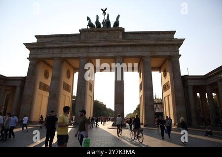 Touristes, deux sur des vélos à l'avant de la porte de Brandebourg avec une sculpture en bronze d'une quadriga sur le dessus, célèbre monument, rétroéclairé par le soleil de l'après-midi. Banque D'Images