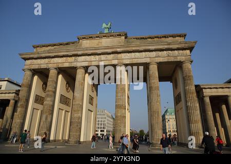 Les touristes marchent à l'arrière de la porte de Brandebourg avec une sculpture en bronze d'une quadriga sur le dessus, célèbre monument allemand, éclairé par le soleil de l'après-midi. Banque D'Images