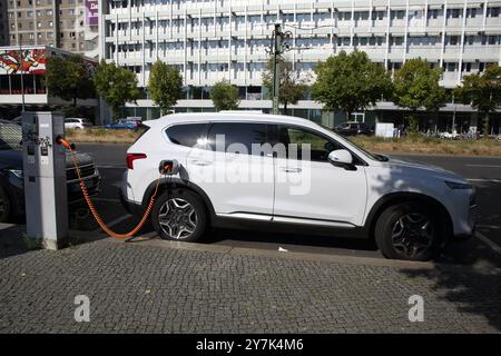 Voiture électrique blanche rechargée avec un câble branché à l'arrière, elle provient d'un chargeur de rue publique installé sur un trottoir berlinois Banque D'Images