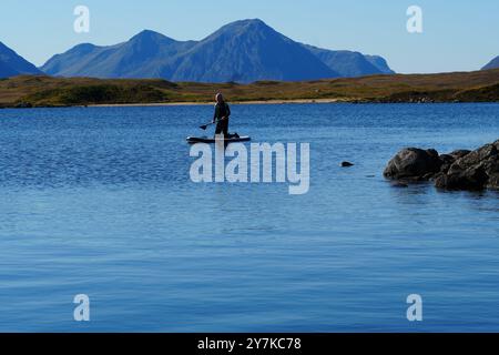 Homme apprenant à paddle board (SUPB) sur le Loch Laidon, avec en toile de fond les montagnes Glen Coe, Rannoch Moor, Écosse, Royaume-Uni Banque D'Images