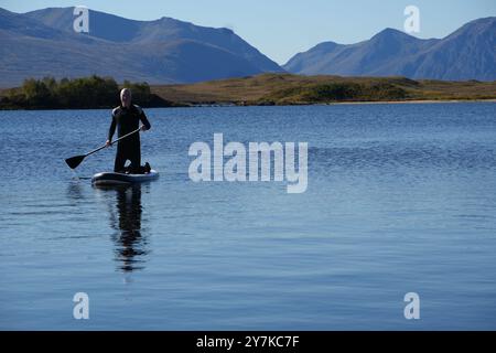 Homme apprenant à paddle board (SUPB) sur le Loch Laidon, avec en toile de fond les montagnes Glen Coe, Rannoch Moor, Écosse, Royaume-Uni Banque D'Images