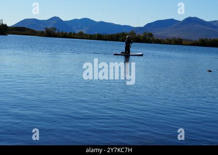 Homme apprenant à paddle board (SUPB) sur le Loch Laidon, avec en toile de fond les montagnes Glen Coe, Rannoch Moor, Écosse, Royaume-Uni Banque D'Images