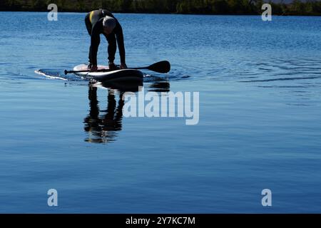 Homme apprenant à paddle board (SUPB) sur le Loch Laidon, avec en toile de fond les montagnes Glen Coe, Rannoch Moor, Écosse, Royaume-Uni Banque D'Images