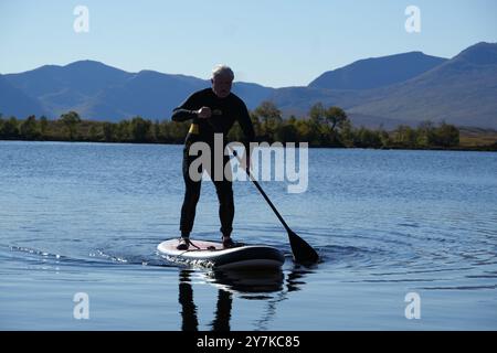 Homme apprenant à paddle board (SUPB) sur le Loch Laidon, avec en toile de fond les montagnes Glen Coe, Rannoch Moor, Écosse, Royaume-Uni Banque D'Images