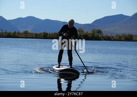 Homme apprenant à paddle board (SUPB) sur le Loch Laidon, avec en toile de fond les montagnes Glen Coe, Rannoch Moor, Écosse, Royaume-Uni Banque D'Images