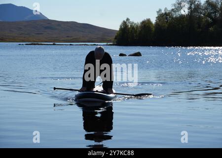 Homme apprenant à paddle board (SUPB) sur le Loch Laidon, avec en toile de fond les montagnes Glen Coe, Rannoch Moor, Écosse, Royaume-Uni Banque D'Images