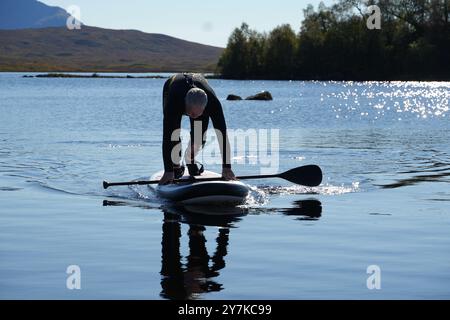 Homme apprenant à paddle board (SUPB) sur le Loch Laidon, avec en toile de fond les montagnes Glen Coe, Rannoch Moor, Écosse, Royaume-Uni Banque D'Images