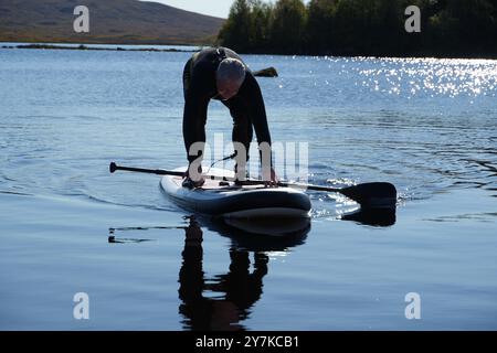 Homme apprenant à paddle board (SUPB) sur le Loch Laidon, avec en toile de fond les montagnes Glen Coe, Rannoch Moor, Écosse, Royaume-Uni Banque D'Images