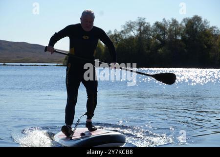 Homme apprenant à paddle board (SUPB) sur le Loch Laidon, avec en toile de fond les montagnes Glen Coe, Rannoch Moor, Écosse, Royaume-Uni Banque D'Images