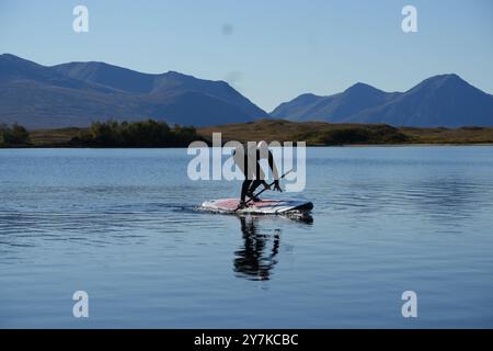 Homme apprenant à paddle board (SUPB) sur le Loch Laidon, avec en toile de fond les montagnes Glen Coe, Rannoch Moor, Écosse, Royaume-Uni Banque D'Images